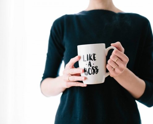 Une femme au t-shirt noir tenant une tasse de café sur laquelle est écrit "like a boss".