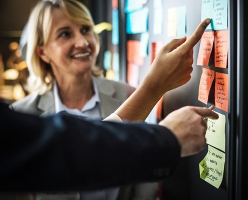 Un tableau avec des post-it regardé par plusieurs personnes.